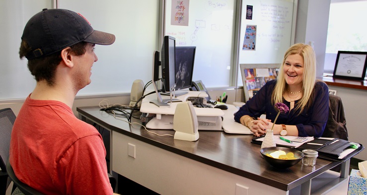 student with red shirt and cap meeting with his academic advisor having a nice conversation